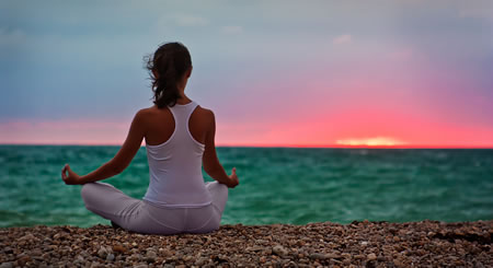 Woman meditating at sunset by ocean